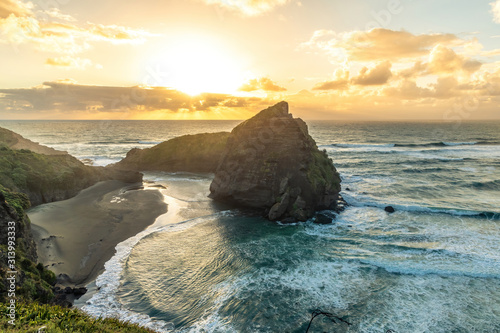 Wide-angle view of Piha beach cove behind Taitomo Island (Camel Rock) in sunset light photo