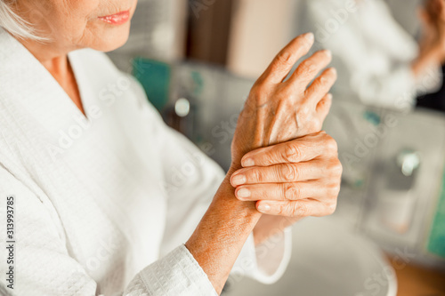 Foto Elderly lady in bathrobe massaging her hands
