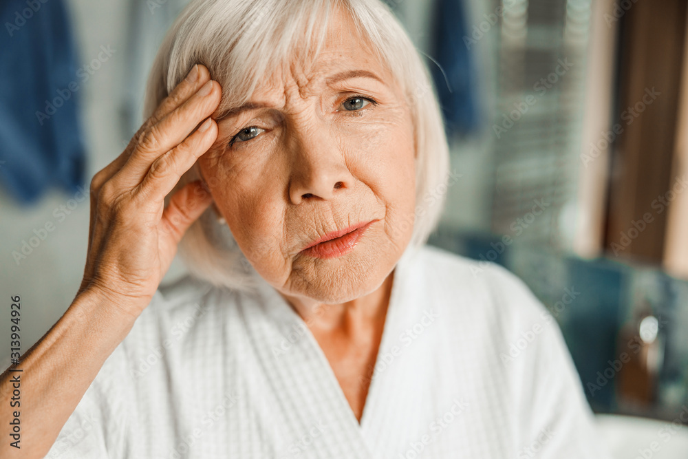 Upset old lady touching forehead and having headache Upset old lady touching forehead and having headache