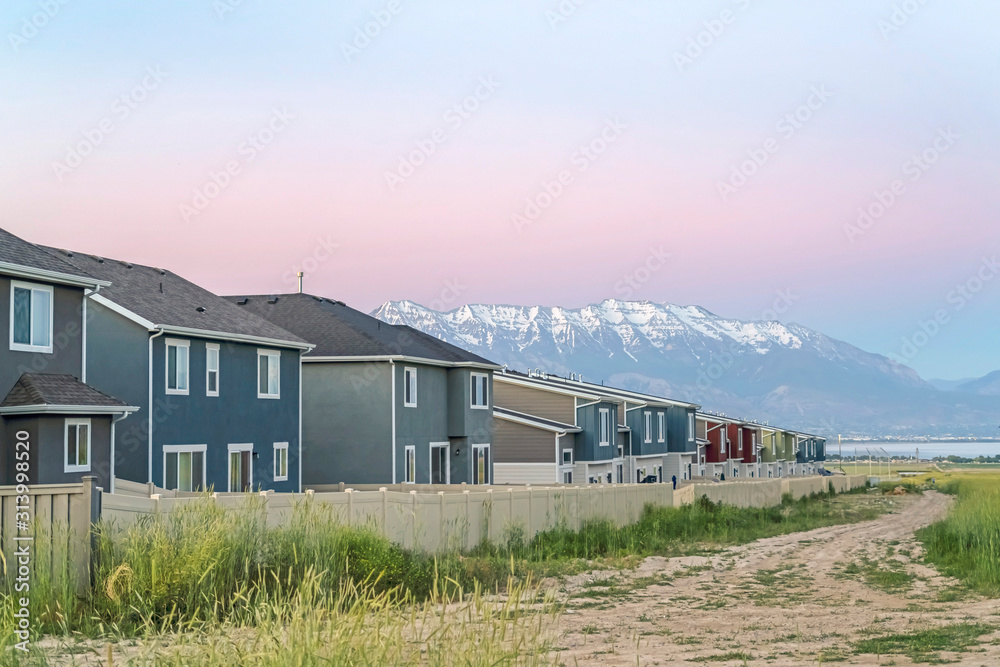 Dirt road along white fences of houses against snow capped mountain at sunset Dirt road along white fences of houses against snow capped mountain at sunset