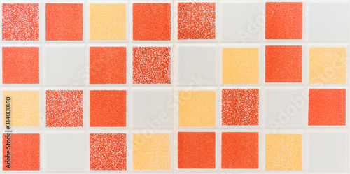 Multiple colored square mosaic tiles texture with white filling decorate the wall in the bathroom.