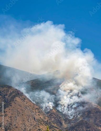 Aerial view of mountain with white smoke from wild forest fire on a sunny day