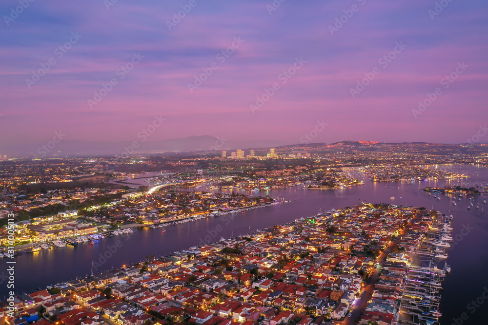 Aerial view over city harbor and bay with water with coastal homes or real estate below after sunset during twilight with colorful sky.