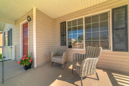 Wicker armchairs on the sunlit front porch of home with brown front door