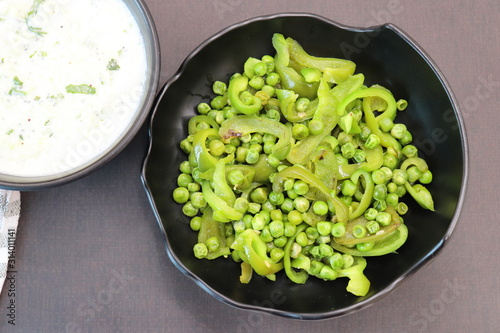 Indian Fresh sauce called Raita with herbs, curd and grated cucumber close-up in a bowl on the table. with some saute vegetables like green bell papers and fresh green peas