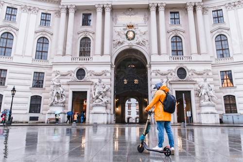 Photography man in yellow raincoat riding by city street at electric scooter