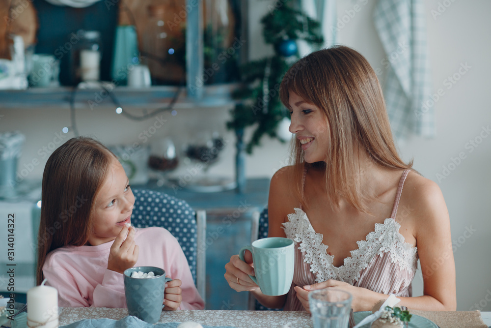 Mother with a little daughter sit and have breakfast at table in  kitchen with cup