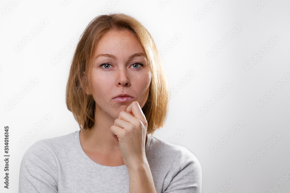 The concept of psychology and emotions. A young blonde woman leans her cheek on her hand, and looks thoughtfully. White background and copy space The concept of psychology and emotions. A young blonde woman leans her cheek on her hand, and looks thoughtfully. White background and copy space