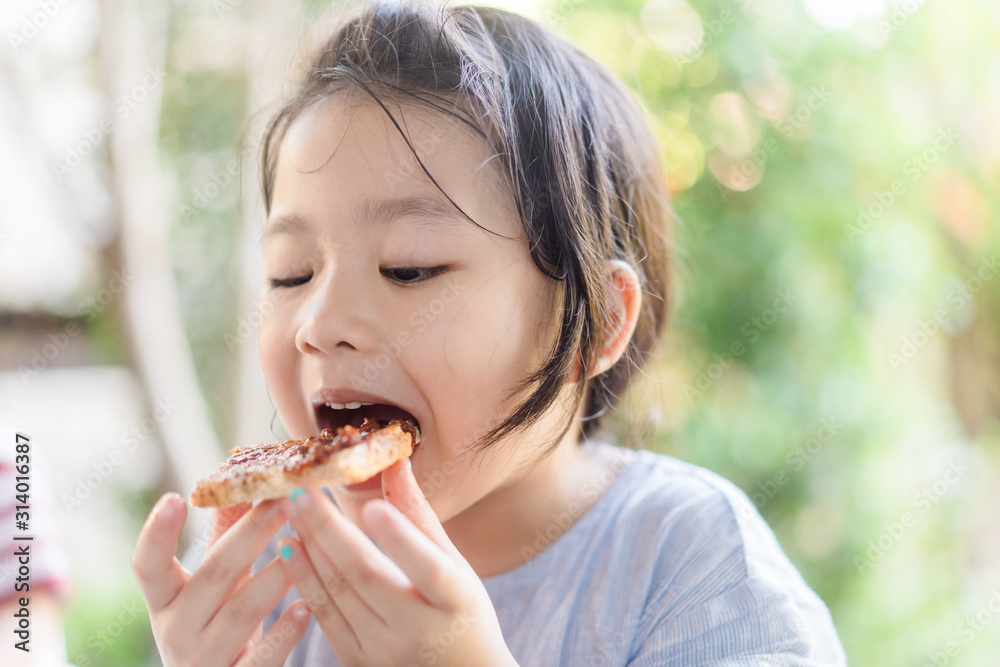 Funny little asian girl eating tasty toasts with strawberry jam spread for breakfast. Hungry face and Delicious face in kid girl. Funny little asian girl eating tasty toasts with strawberry jam spread for breakfast. Hungry face and Delicious face in kid girl.