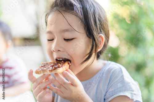 Funny little asian girl eating tasty toasts with strawberry jam spread for breakfast. Hungry face and Delicious face in kid girl.
