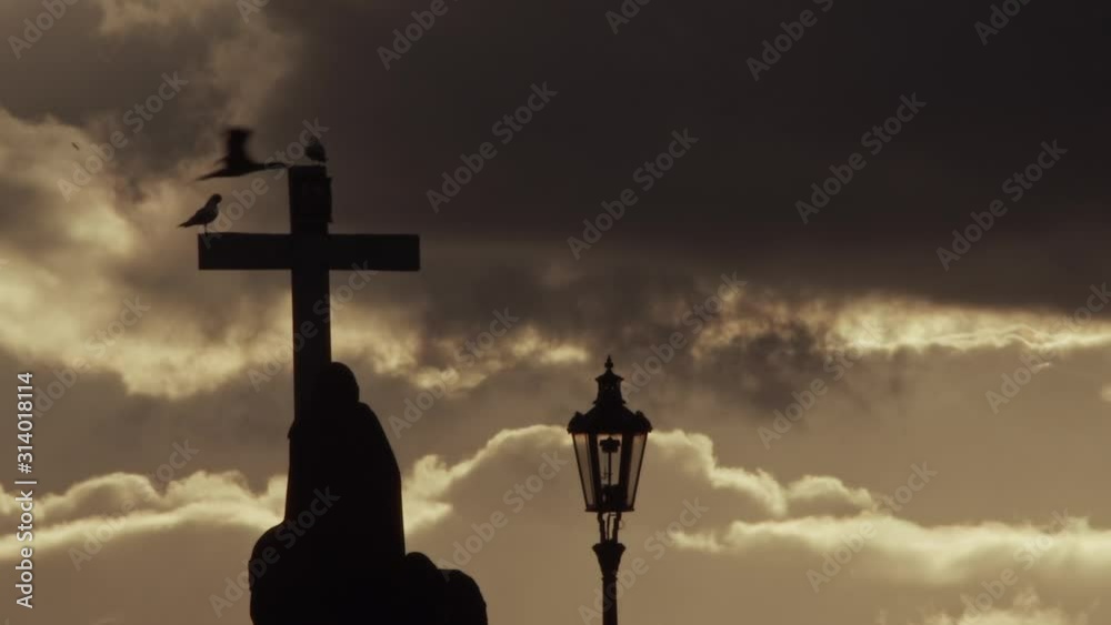 Birds perch on cross statute on Charles Bridge in Prague, silhouette Birds perch on cross statute on Charles Bridge in Prague, silhouette