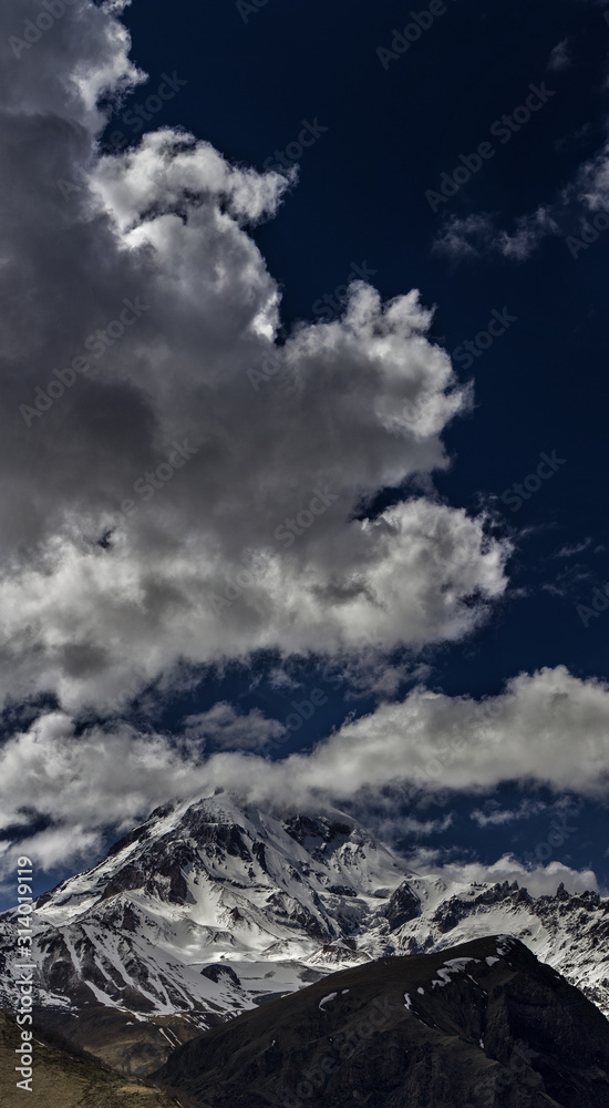 Clouds in the blue sky hit the top of the magnificent Kazbek. Mountain landscape panorama.