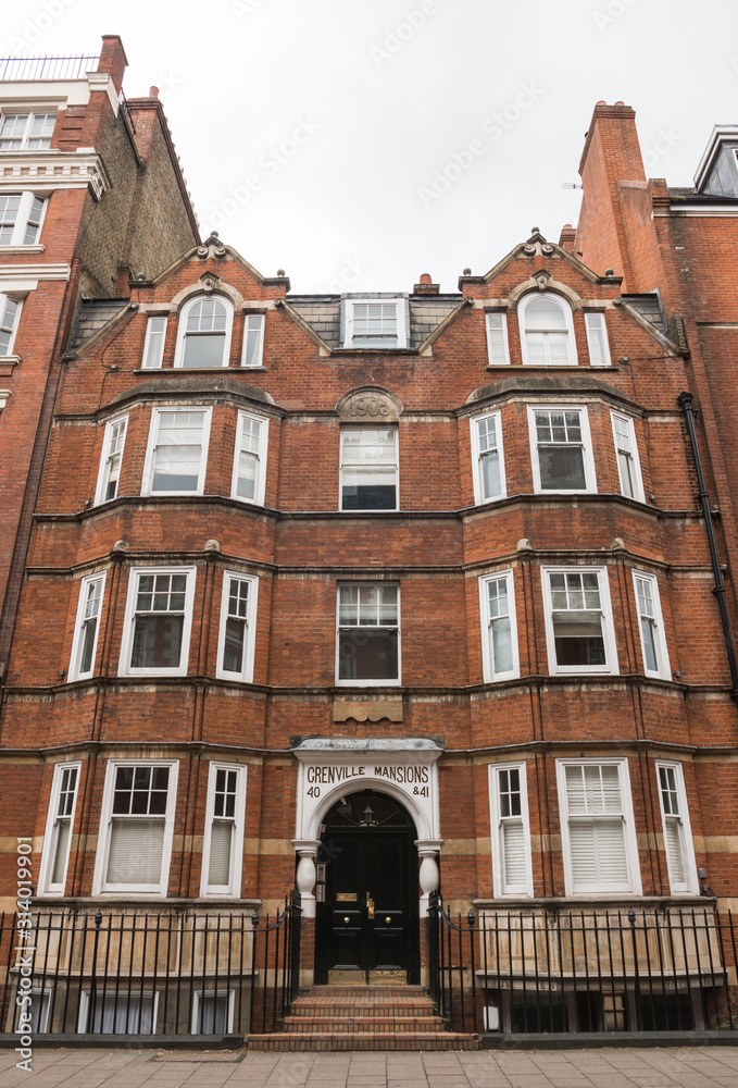 Fototapeta premium Grenville mansions, Hunter Street, London, United Kingdom, England. June 2019. Beautiful vertical shot of this red brick building (black metal fence in front of it). Cloudy day in the english capital