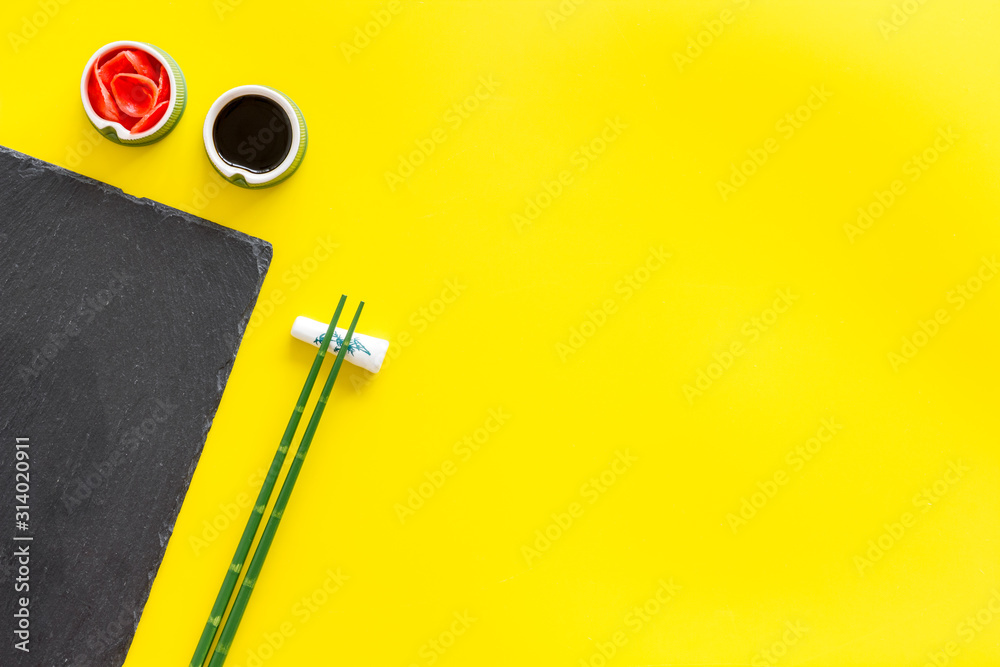 Table served for eating sushi. Chopsticks, small bowls with ginger and sause, mat on yellow background top-down copy space Table served for eating sushi. Chopsticks, small bowls with ginger and sause, mat on yellow background top-down copy space