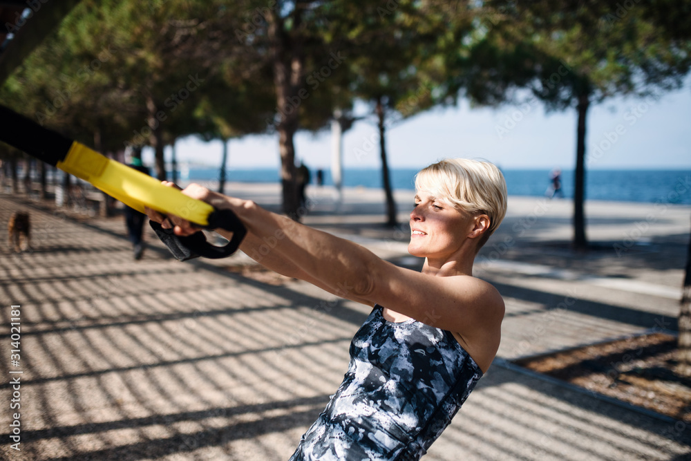 Fototapeta premium A young sportswoman doing exercise with TRX fitness straps outdoors.