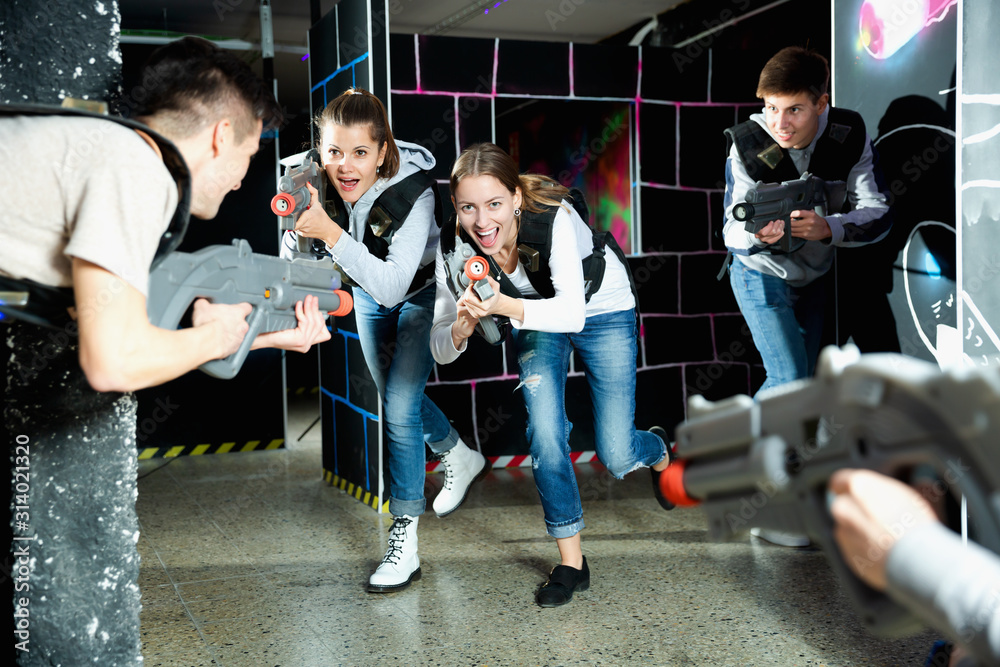 Modern young people with laser pistols playing laser tag on dark labyrinth