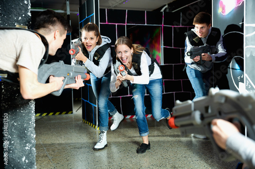 Modern young people with laser pistols playing laser tag on dark labyrinth