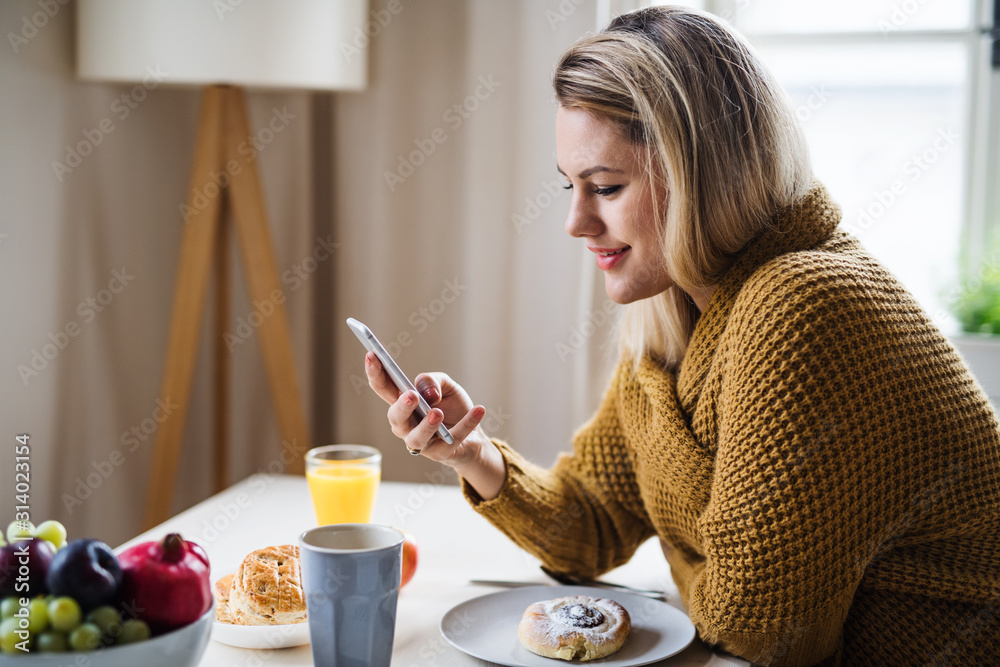 Young woman sitting at the table indoors at home, using smartphone. Young woman sitting at the table indoors at home, using smartphone.