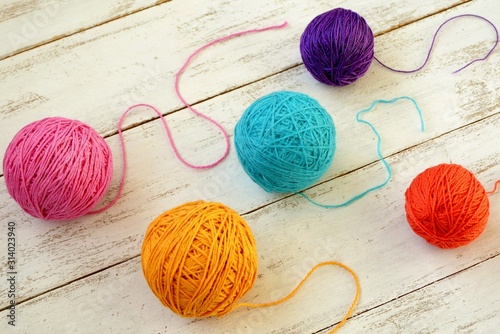 Balls of multicolored yarn on white wooden background.
