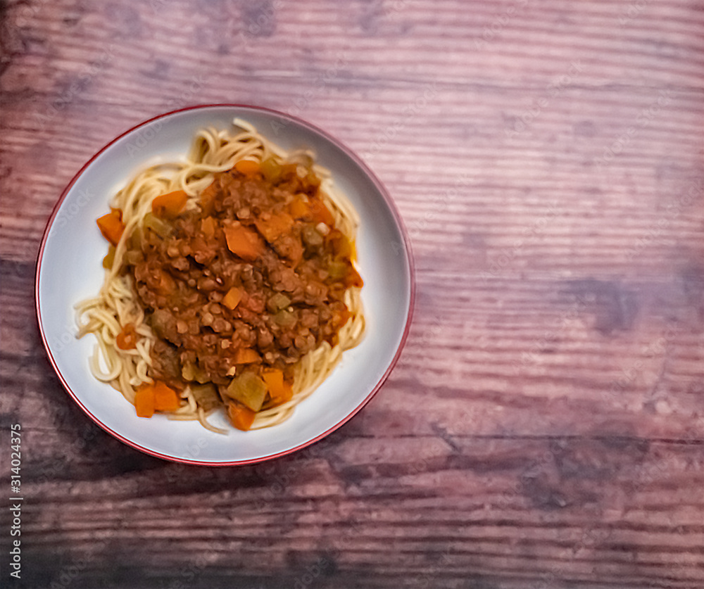 Flat lay of a bowl of lentil spaghetti bolognese on a wooden background with copy space Flat lay of a bowl of lentil spaghetti bolognese on a wooden background with copy space