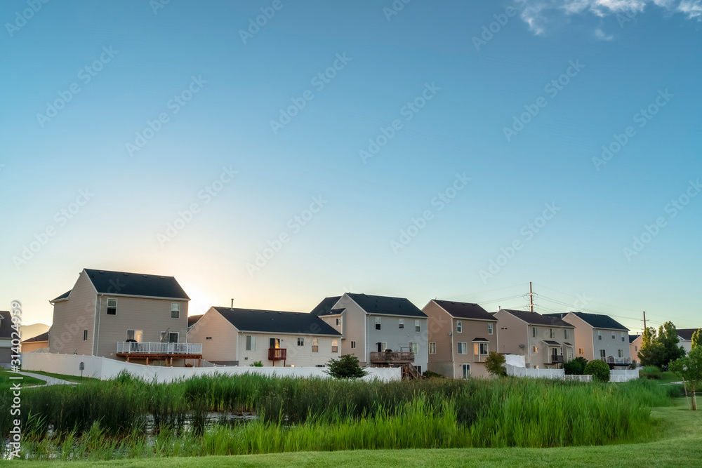 Facade of houses in the suburb with view of green grassy terrain and shiny pond