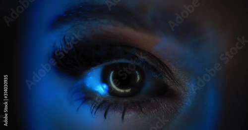 Close up of a woman's eye with beautiful party make up, long black eyelashes, opening in a dark blue lighting. Slow motion, dark studio light. BMPCC 4K