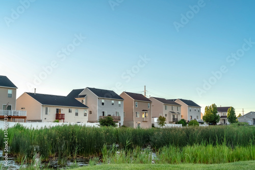 Green grasses and pond at a scenic park with houses and blue sky background