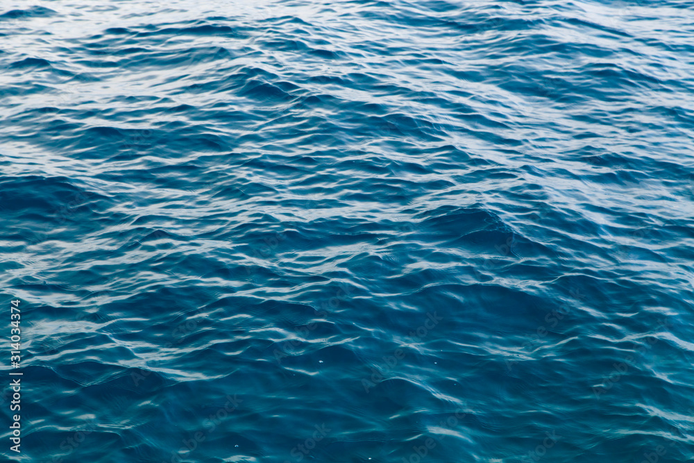 Clear water texture in blue. Background of the ocean and the sea backlit by the sun. Clear water texture in blue. Background of the ocean and the sea backlit by the sun.