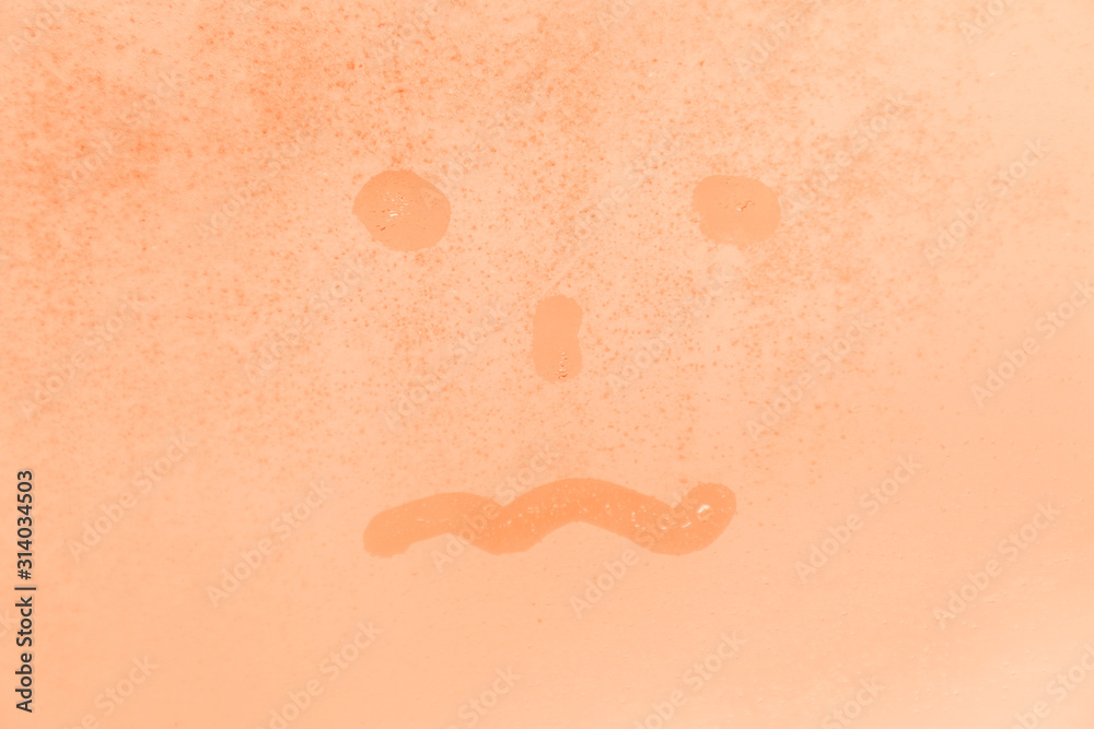 Fototapeta premium The picture or figure of the scared or tired face on the orange or pink evening or morning window glass with drops 