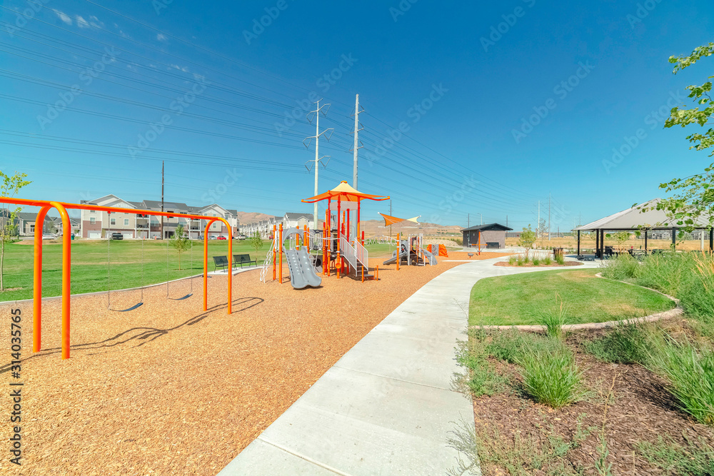 Swings and slides at a playground with pathways and pavilion against blue sky