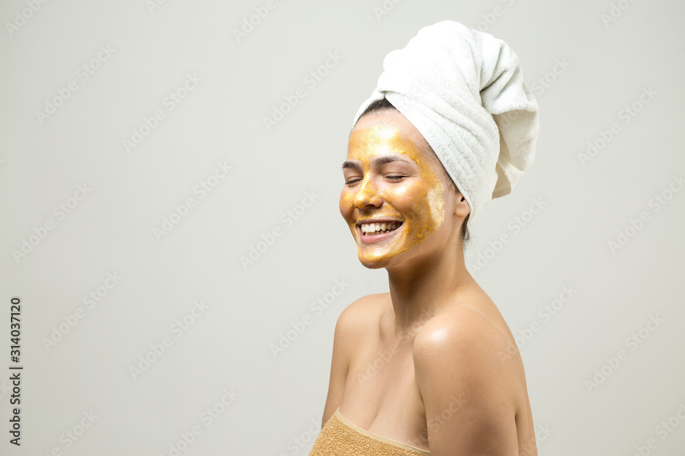 Beauty portrait of woman in white towel on head with gold nourishing mask on face. Skincare cleansing eco organic cosmetic spa relax concept. Beauty portrait of woman in white towel on head with gold nourishing mask on face. Skincare cleansing eco organic cosmetic spa relax concept.