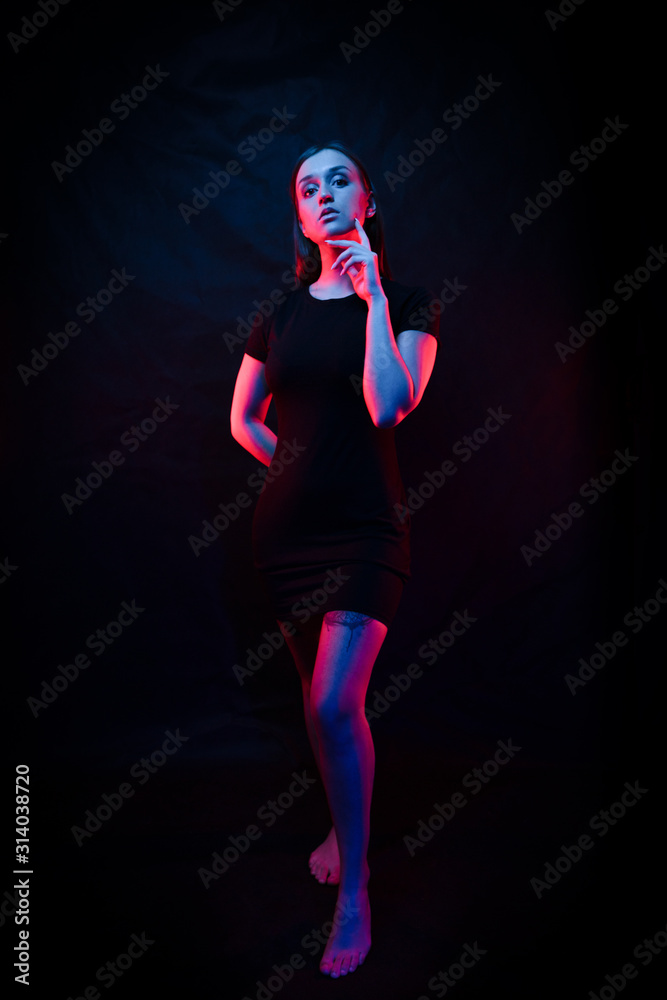 beautiful girl in a black dress. light of colored lamps of blue red colors. Girl stands in full growth. on a black background. Fashion contemporary neon portrait. Adorable fashionable sexy model girl. beautiful girl in a black dress. light of colored lamps of blue red colors. Girl stands in full growth. on a black background. Fashion contemporary neon portrait. Adorable fashionable sexy model girl.