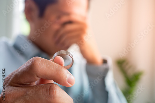 Image of husband crying sadly holding a wedding ring after an argument with his wife and deciding to separate.