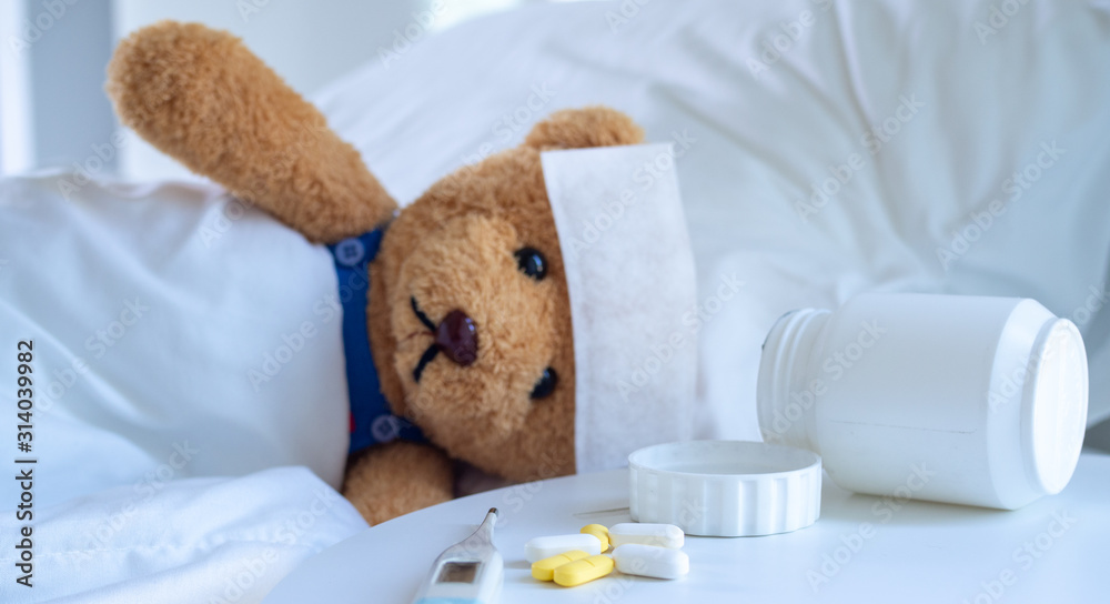 Φωτογραφία The teddy bear and the fever-reducing patch lie on the bed in a white-tone bed next to a medicine table and body temperature monitor