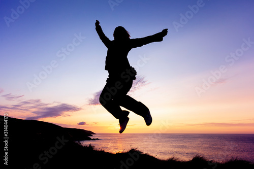 Wallpaper Mural Silhouette of woman jumping for joy on coastal clifftops at sunset Torontodigital.ca