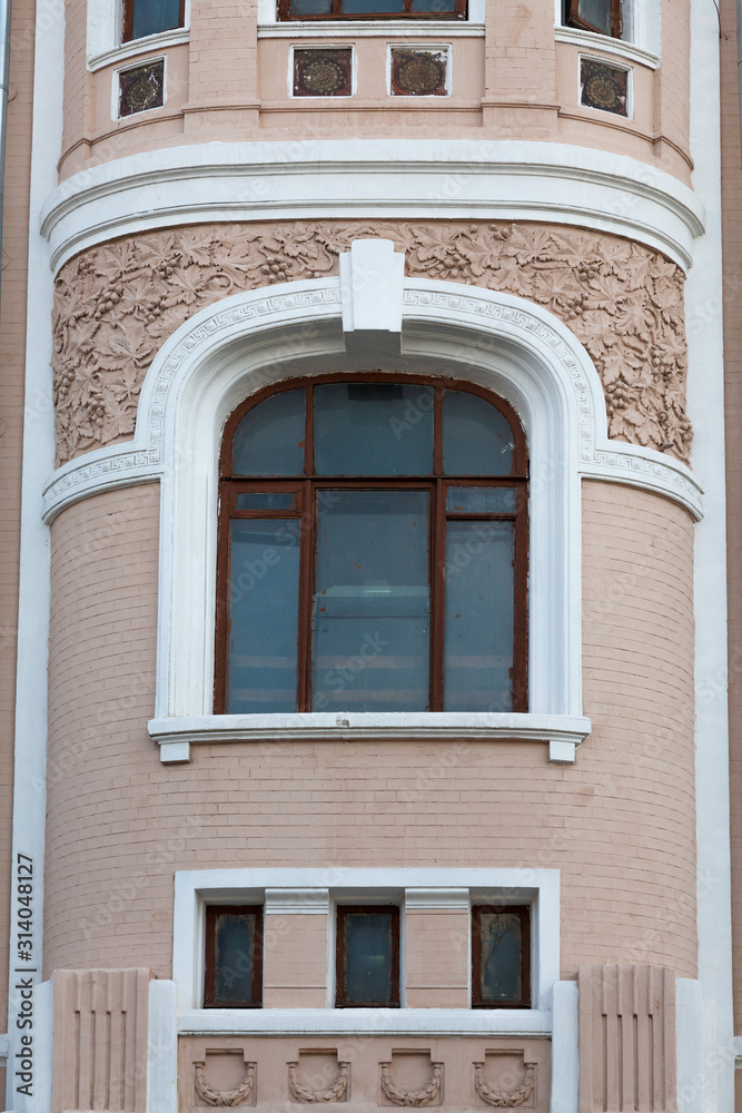 Fragment of the facade of an old building with a window framed by a twisted floral pattern