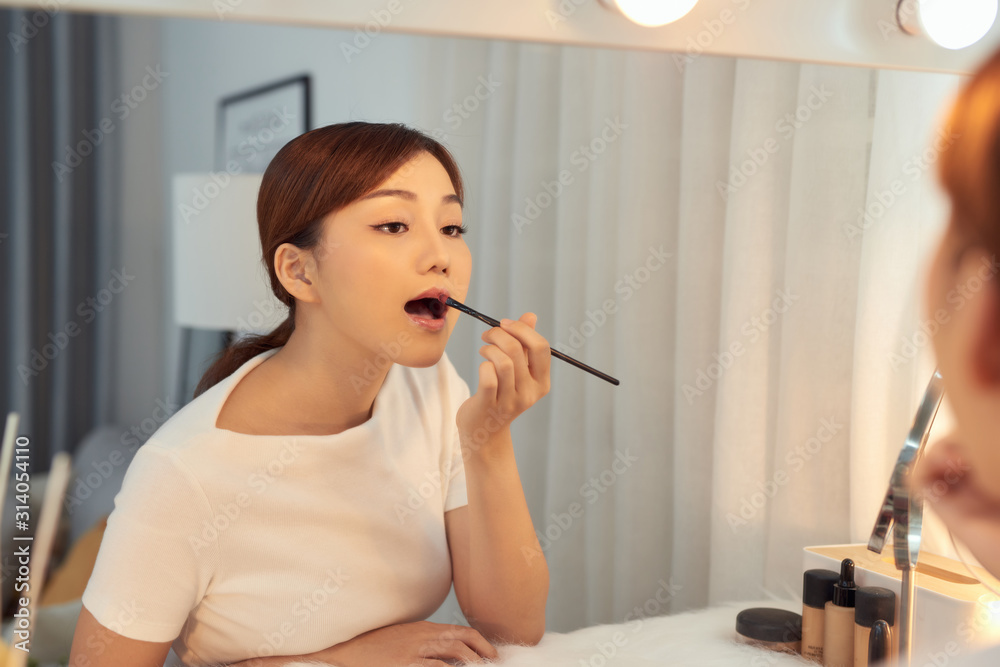 Beautiful Asian girl applying lipstick watching in mirror at makeup table Beautiful Asian girl applying lipstick watching in mirror at makeup table