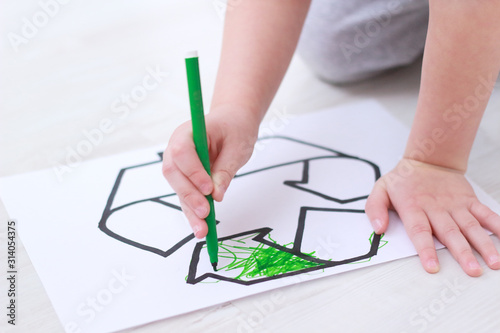 little boy colours with green felt-tip pen a recycling sign on the floor in the playroom. Ecology and environmental protection concept. selective focus