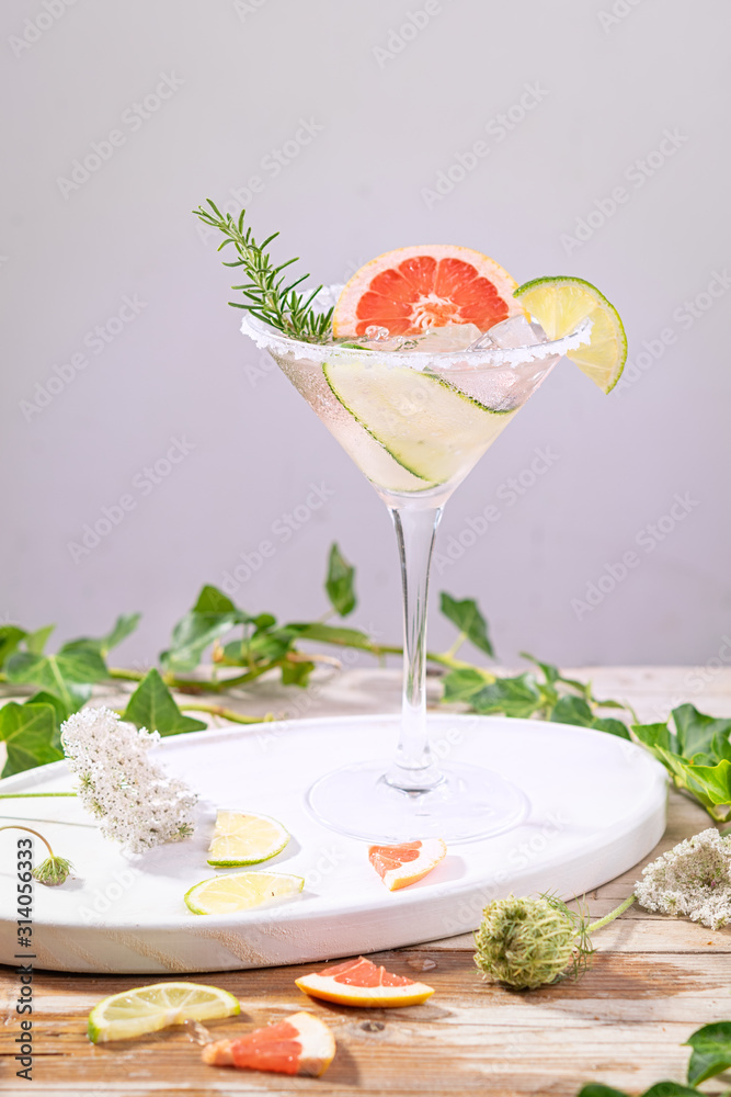 Alcohol drink, gin tonic cocktail with grapefruit, cucumber, rosemary, lime, refreshing, cold drinks with ice on a rustic table. Summer garden party, still life with artistic shadows. Copy space.