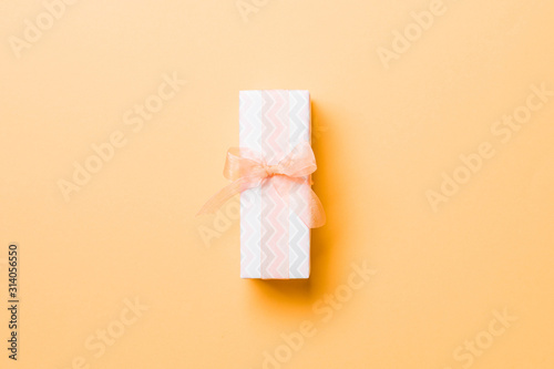 wrapped Christmas or other holiday handmade present in paper with orange ribbon on orange background. Present box, decoration of gift on colored table, top view with copy space