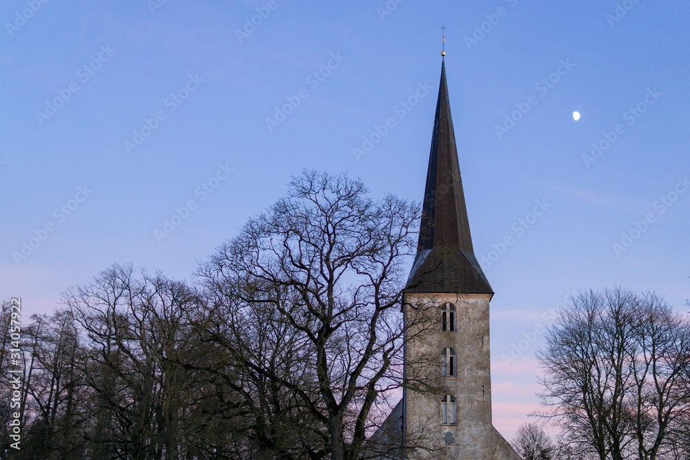 Lutheran Church in the evening, beautiful sunset with moon, trees, sky. Jaunpils, Latvia. Copy space.