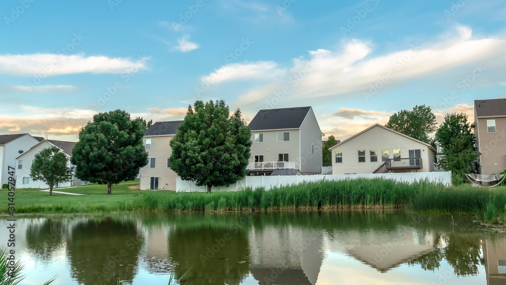 Pano frame Scenic suburban landscape with homes and cloudy sky reflected on a shiny pond Pano frame Scenic suburban landscape with homes and cloudy sky reflected on a shiny pond
