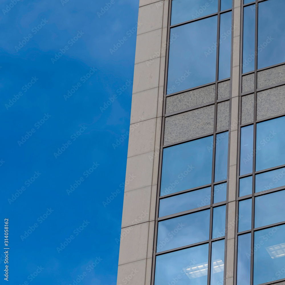 Obraz premium Square frame Focus on a modern building exterior with glass windows reflecting the blue sky