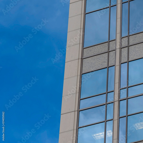 Square frame Focus on a modern building exterior with glass windows reflecting the blue sky