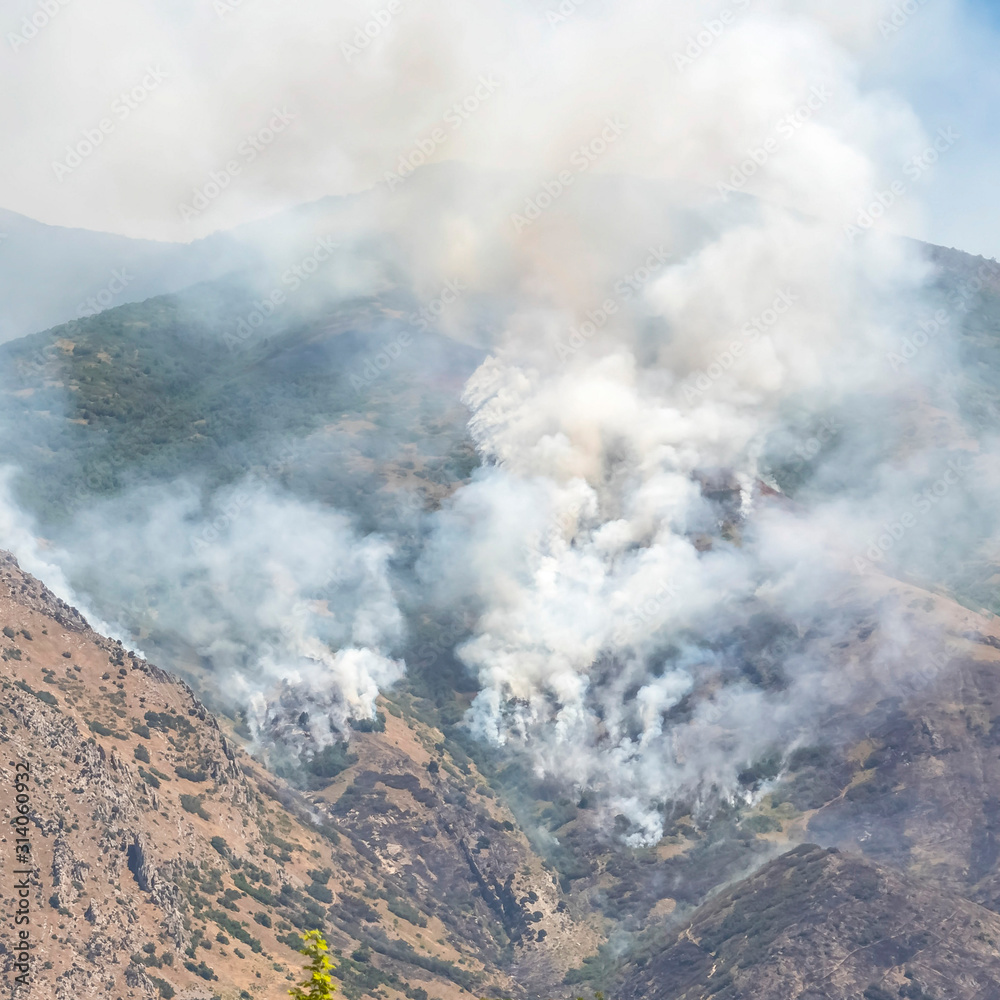 Square Nature landscape with puffs of white smoke rising from mountain forest fire