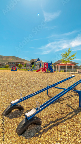Vertical frame Bright blue see saw at a playground with Timpanogos Mountains and blue sky view © Jason