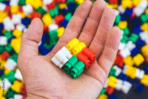 Hand with colorful plastic bricks and details of toys on a colorful background