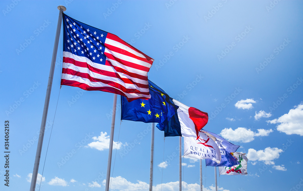 the flags of the United States of America, Europe and France floating in the wind over the blue sky the flags of the United States of America, Europe and France floating in the wind over the blue sky