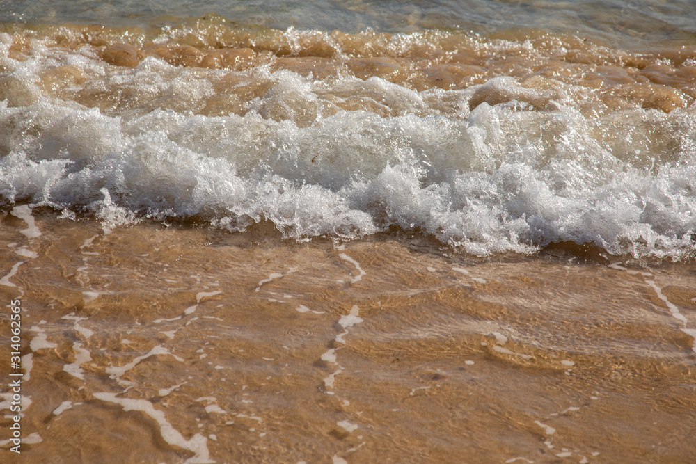 Waves breaking on an empty sand beach and spalsh producing foam - travel holiday vacation summer sun - splashing water - wavy golden yellow sand background - empty space Waves breaking on an empty sand beach and spalsh producing foam - travel holiday vacation summer sun - splashing water - wavy golden yellow sand background - empty space