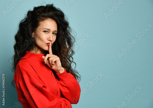 Curly hair woman showing hush quite tsss sign with red lips and sweater  photo